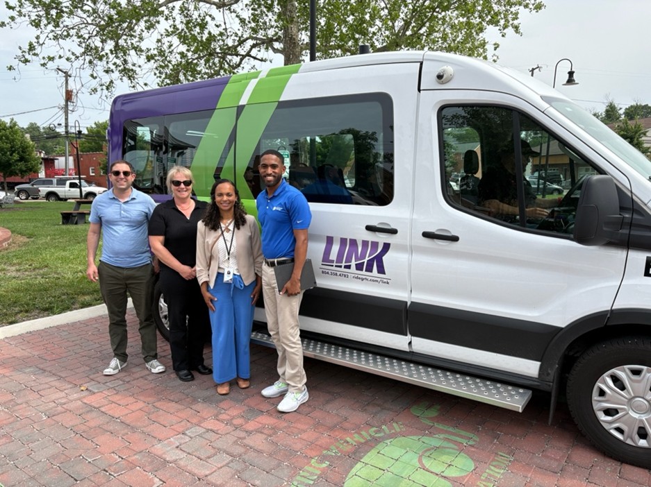 four people standing in front of an electric transit van